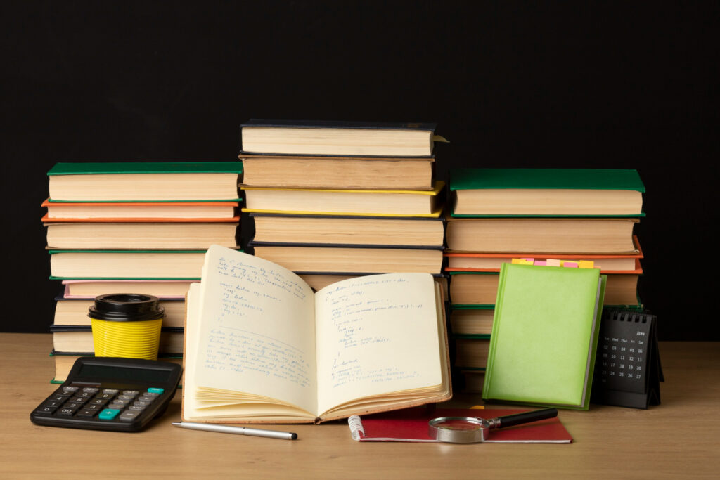 A stack of books beside a calculator on a wooden table, suggesting a study or academic environment.
