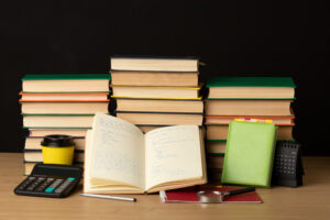 A stack of books beside a calculator on a wooden table, suggesting a study or academic environment.