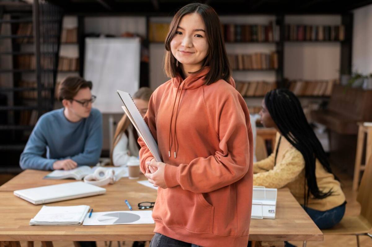 A group of young adults collaborates around a wooden table in a cozy study room filled with shelves of books.