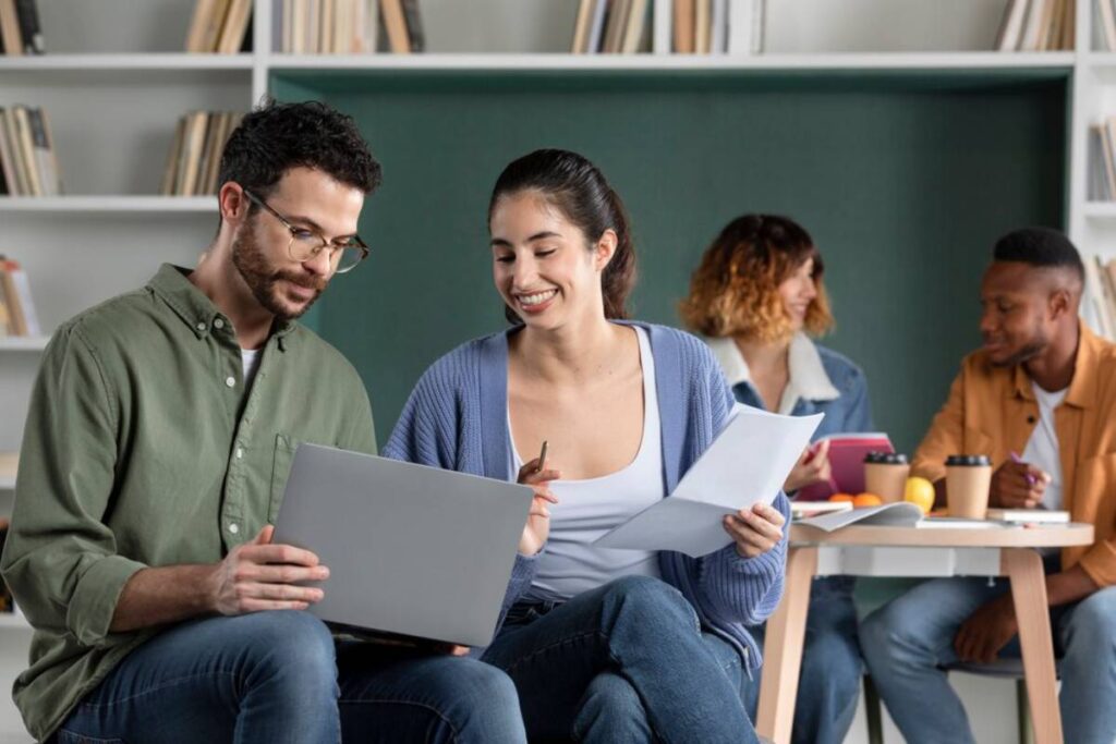 A group of young adults collaborates on a project, reviewing documents and a laptop in a cozy, book-filled setting.
