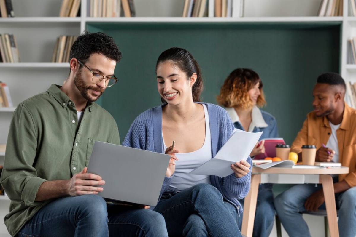 A group of young adults collaborates on a project, reviewing documents and a laptop in a cozy, book-filled setting.