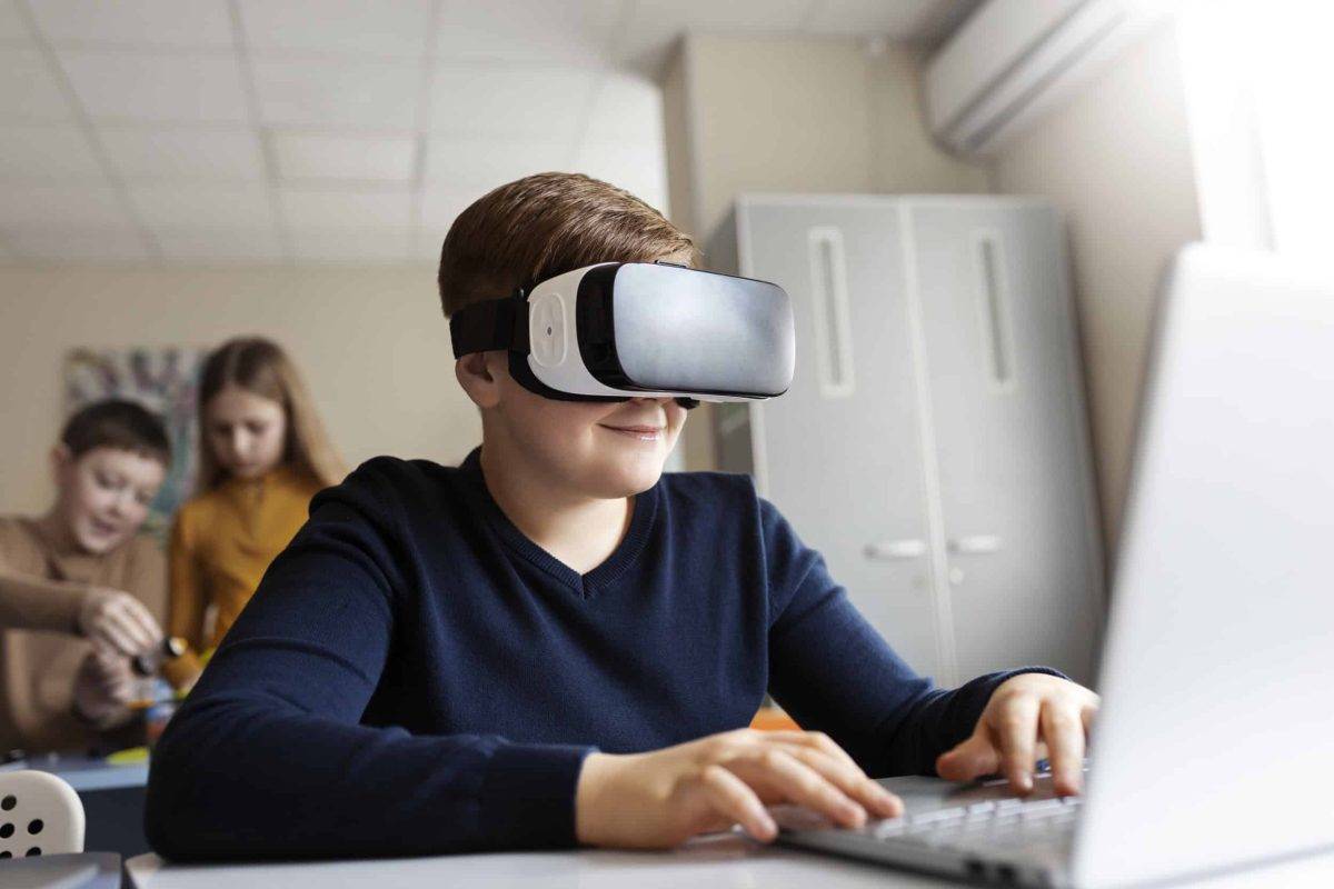 A student wearing a virtual reality headset interacts with a laptop in a modern classroom setting.