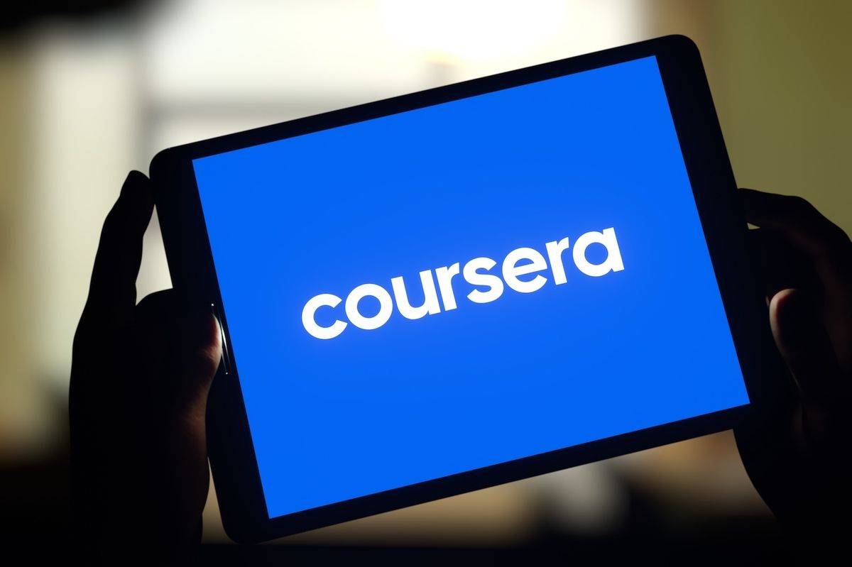 A person holds a tablet displaying the Coursera logo on a bright blue background.