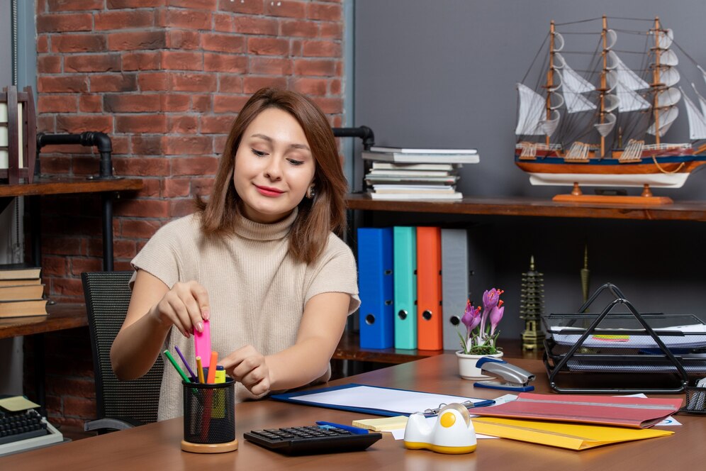 An organized office desk features a variety of colorful stationery, books, folders, and a decorative ship model, creating a vibrant workspace.