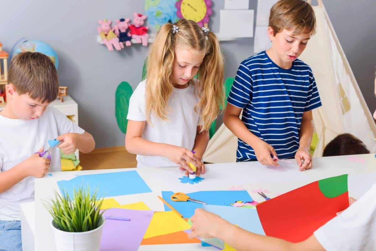 Children engaged in a colorful arts and crafts activity, cutting and assembling various paper shapes at a table.