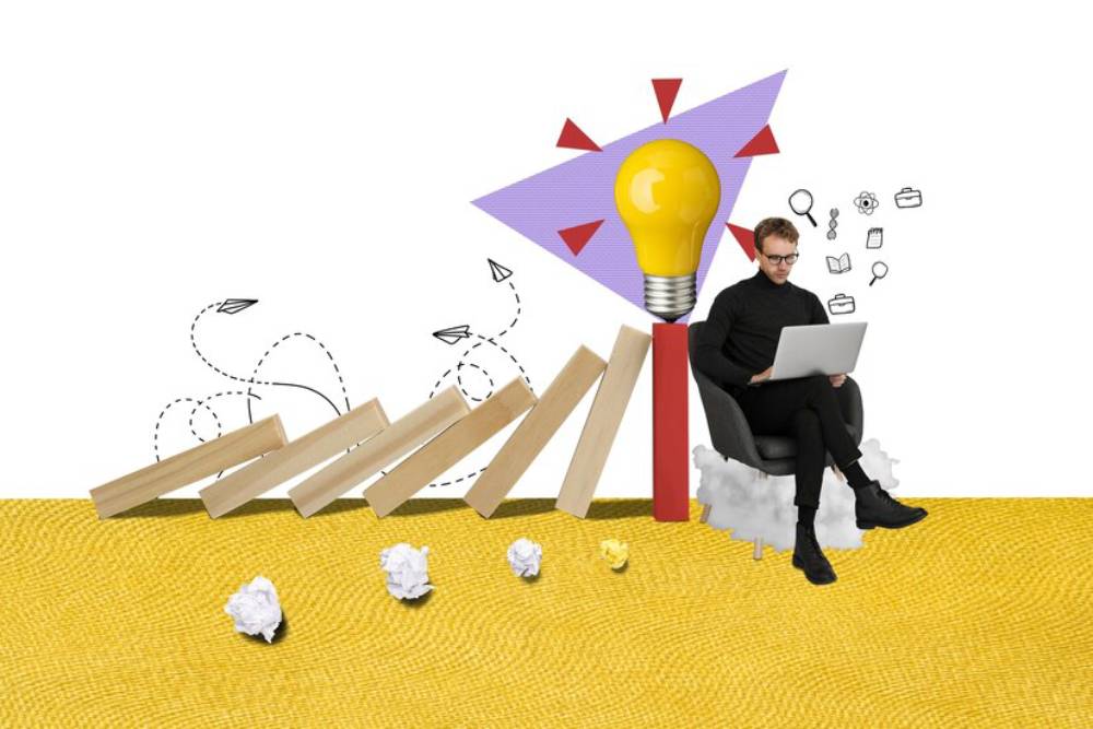 A person sits in a chair with a laptop, surrounded by scattered paper and wooden blocks, symbolizing problem-solving skills