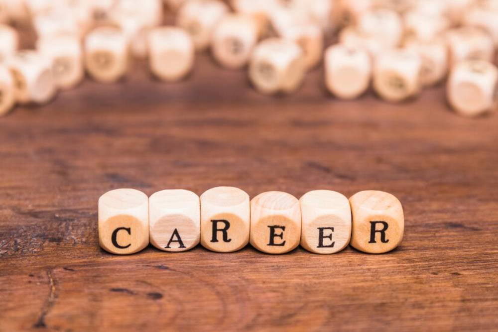 Wooden blocks spell out CAREER on a wooden surface, surrounded by scattered similar blocks.