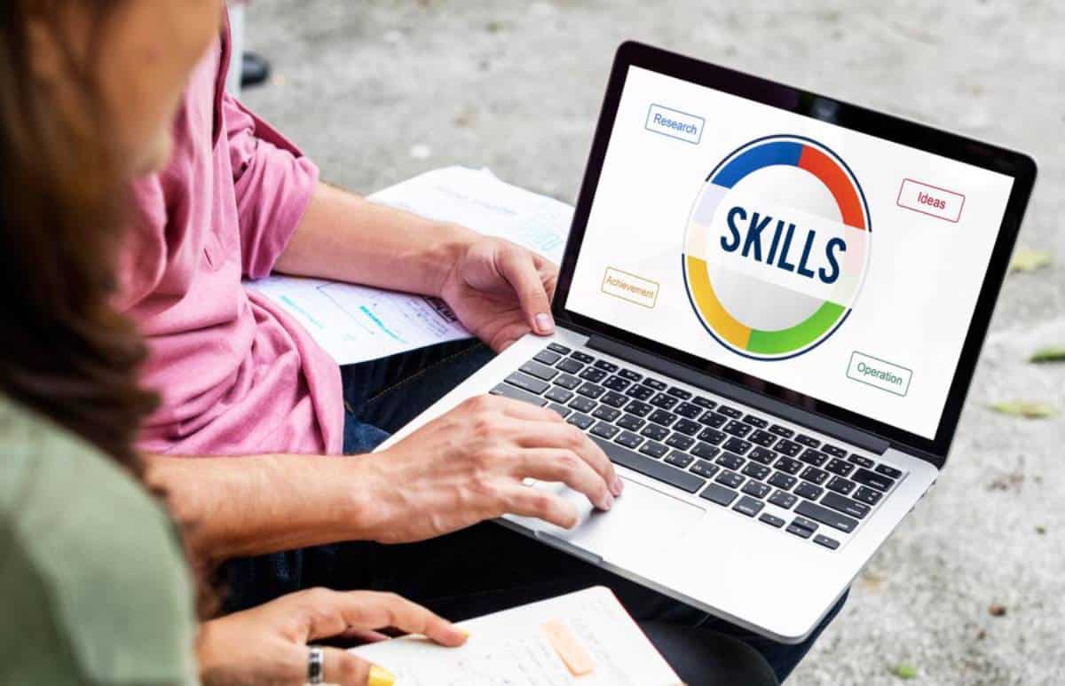 A person typing on a laptop displaying a colorful "Skills" graphic with labels for Research, Ideas, Achievement, and Operation.